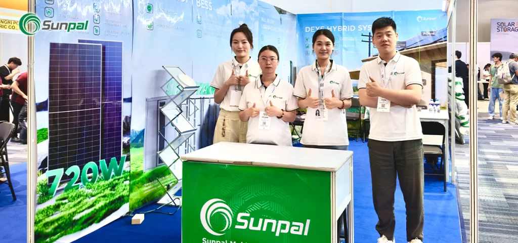 Four Sunpal team members giving a thumbs-up at their green and blue themed exhibition booth displaying 720W TOPCon solar panels.